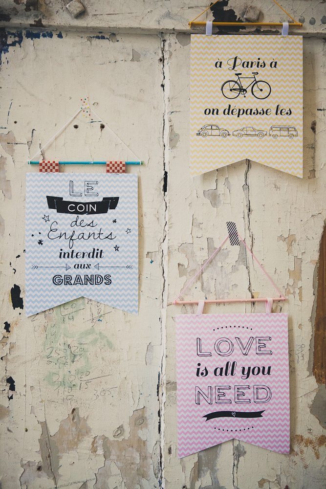 Trois bannières DIY colorées et illustrées suspendues sur un mur blanc rustique et écaillé.