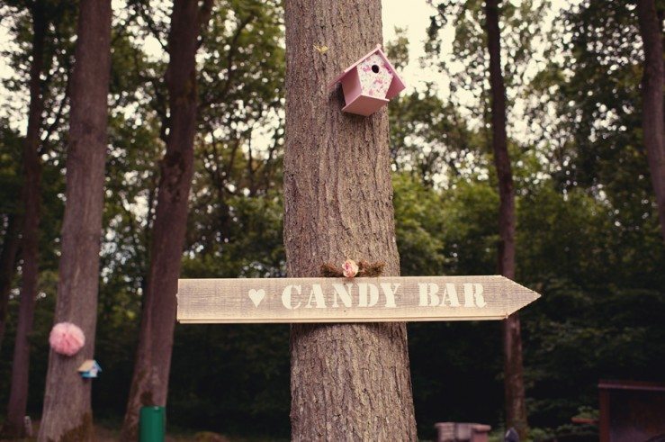 Un panneau en bois indiquant l'emplacement d'une barre de sucre dans un décor charmant de forêt.