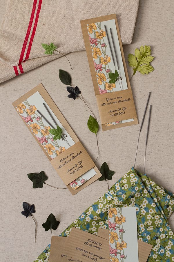 Étincelles de mariage dans des étuis en kraft illustrés de fleurs, posées sur un tissu floral et un linge naturel.
