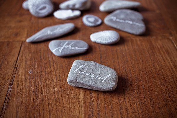 Galets blancs et gris gravés de prénoms, disposés sur une table en bois rustique.