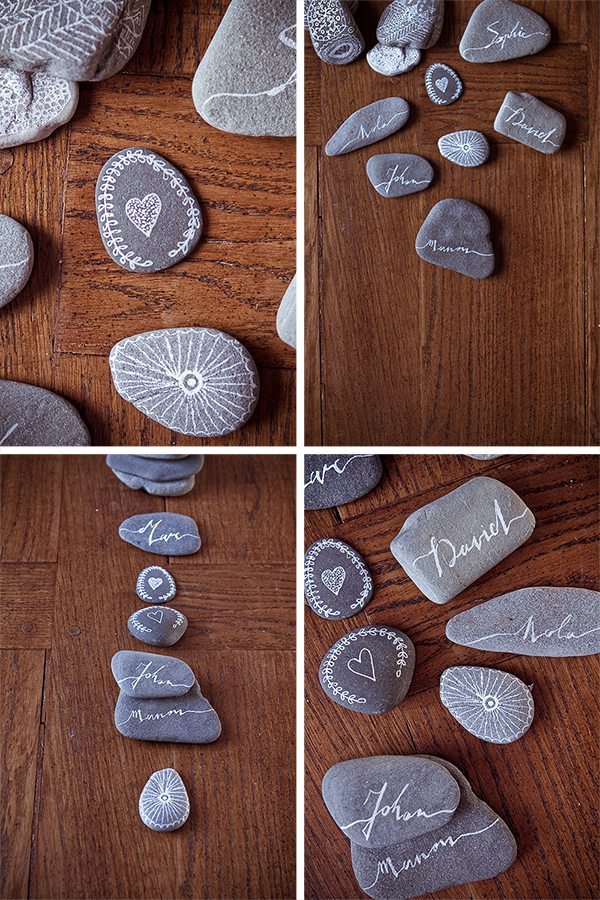 Galets gris décorés de motifs blancs et de prénoms calligraphiés, disposés sur un parquet en bois sombre.