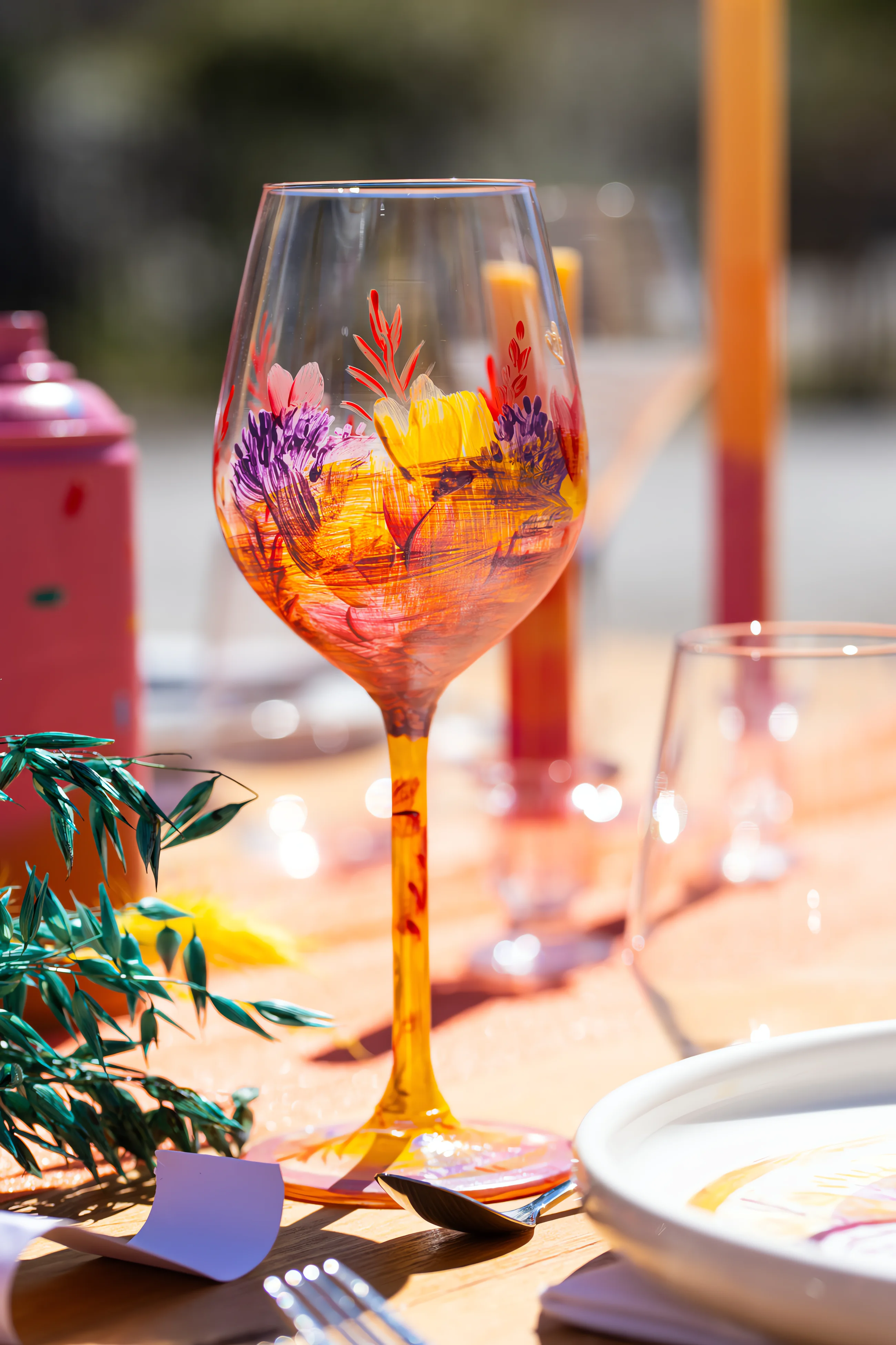 Verre à pied coloré aux motifs street art orange et violet sur une table de mariage ensoleillée.