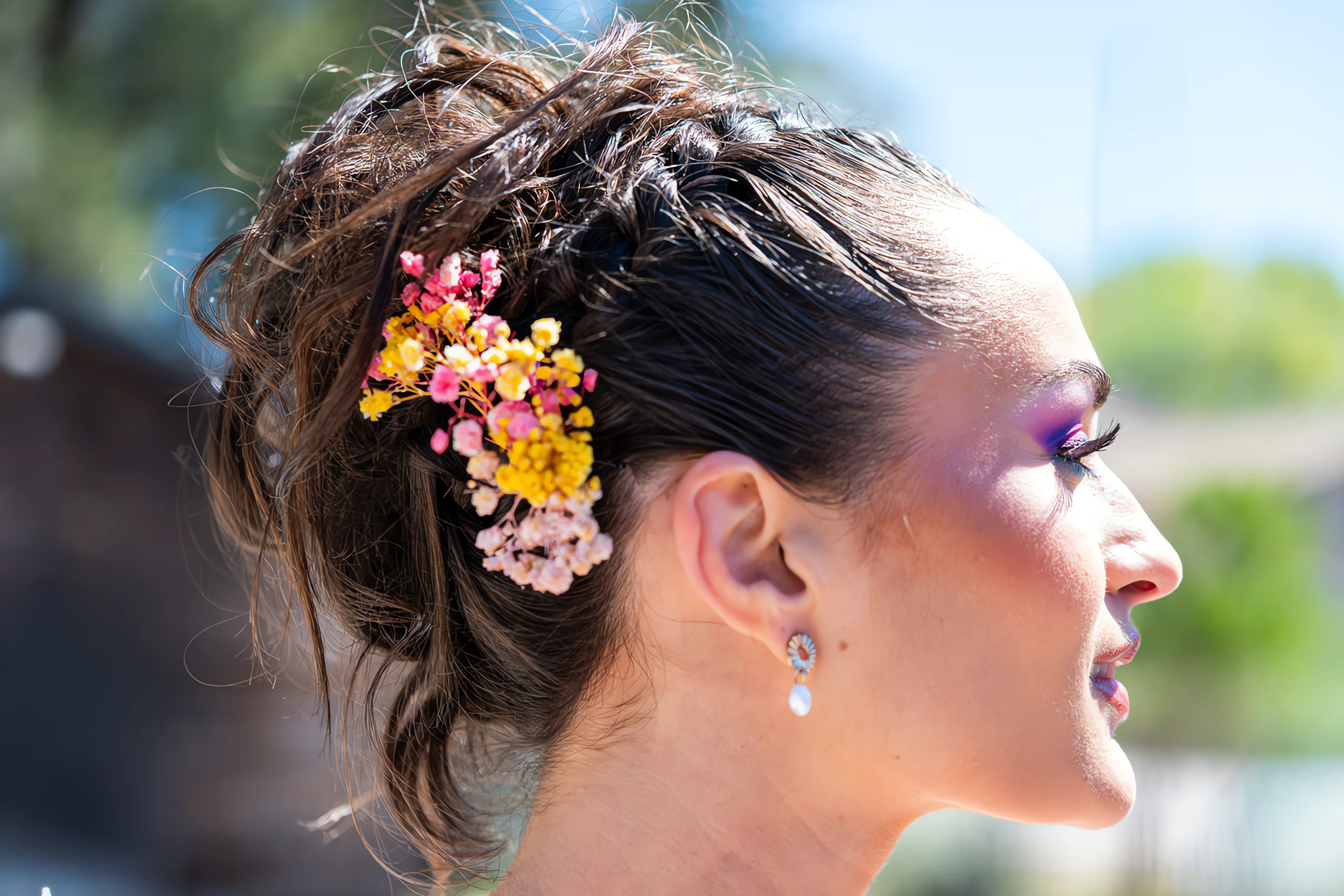 Profil d'une mariée au chignon tressé orné de fleurs colorées, avec un maquillage audacieux et lumineux.