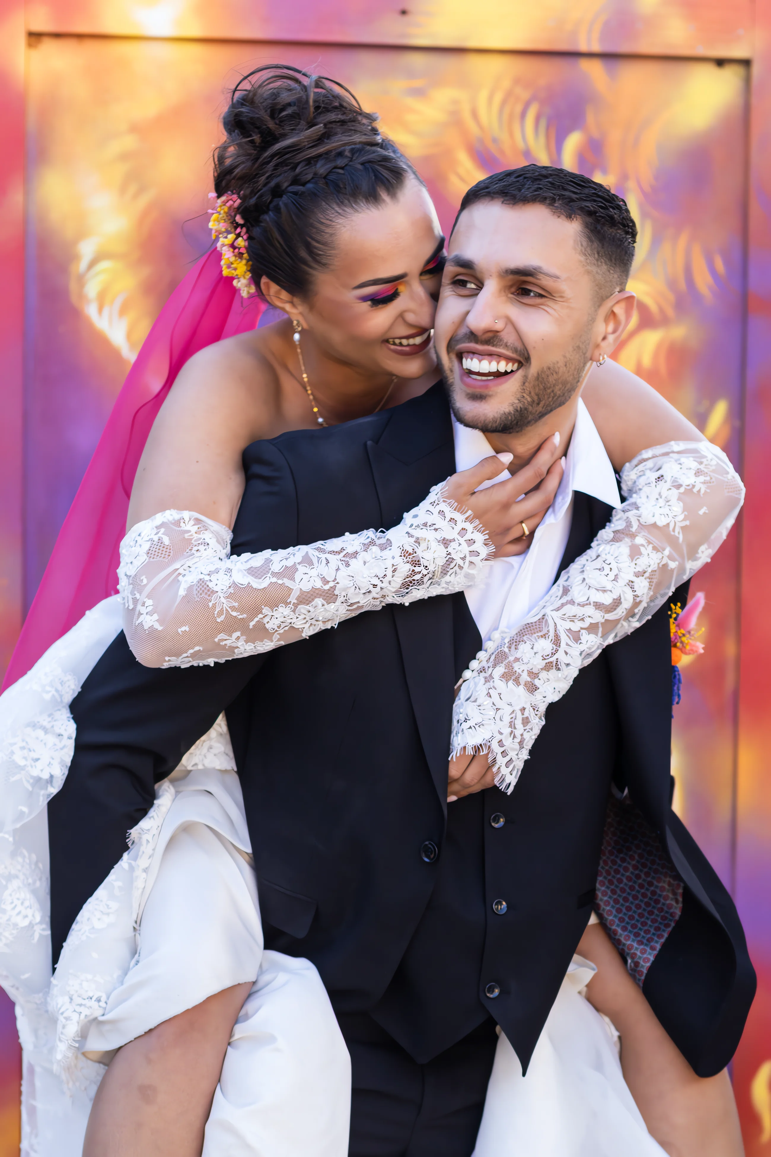 Jeune couple marié s'enlaçant joyeusement devant un mur coloré en street art.