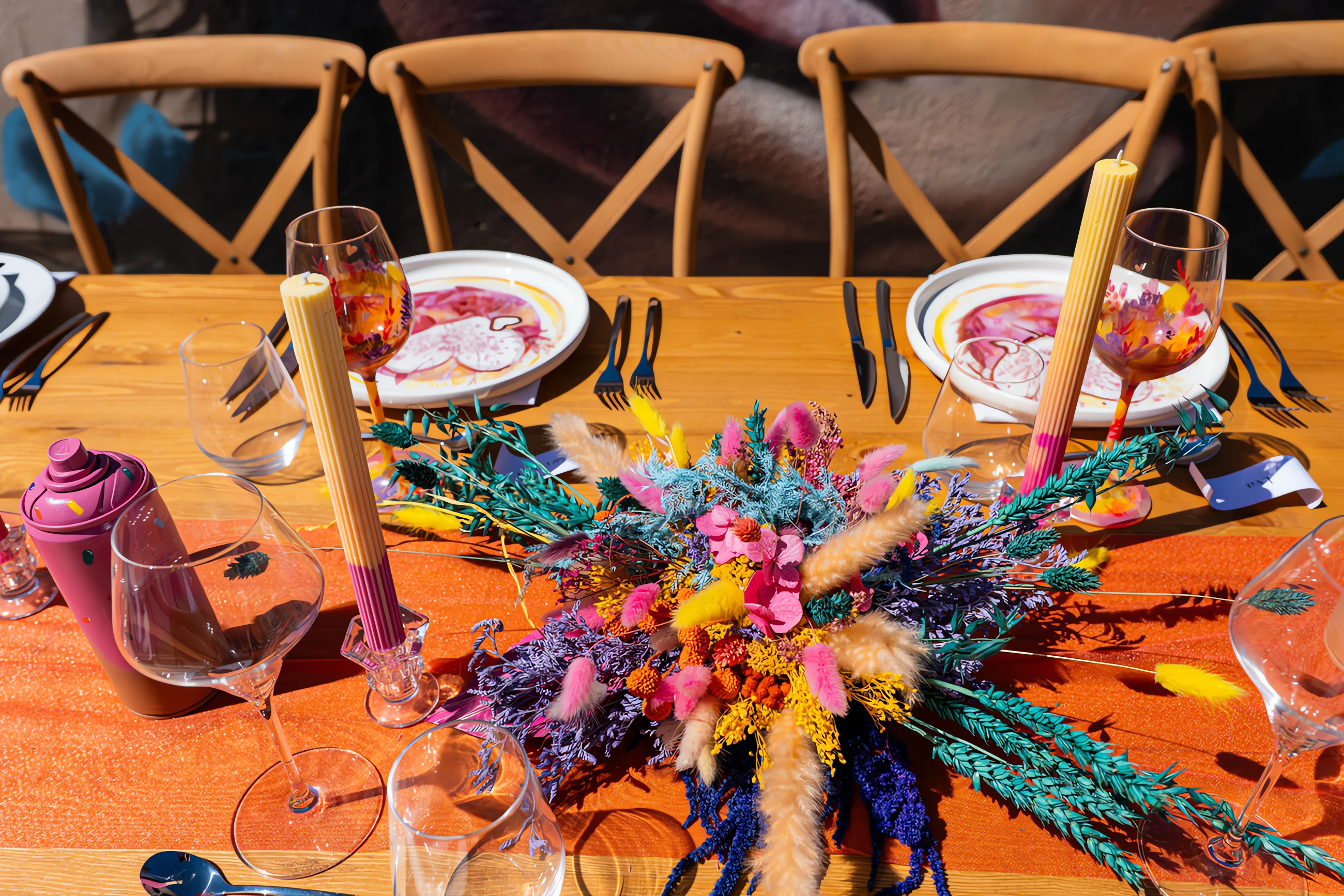 Table de mariage colorée avec fleurs séchées, vaisselle artistique et bougies sur un nappe orange vif.