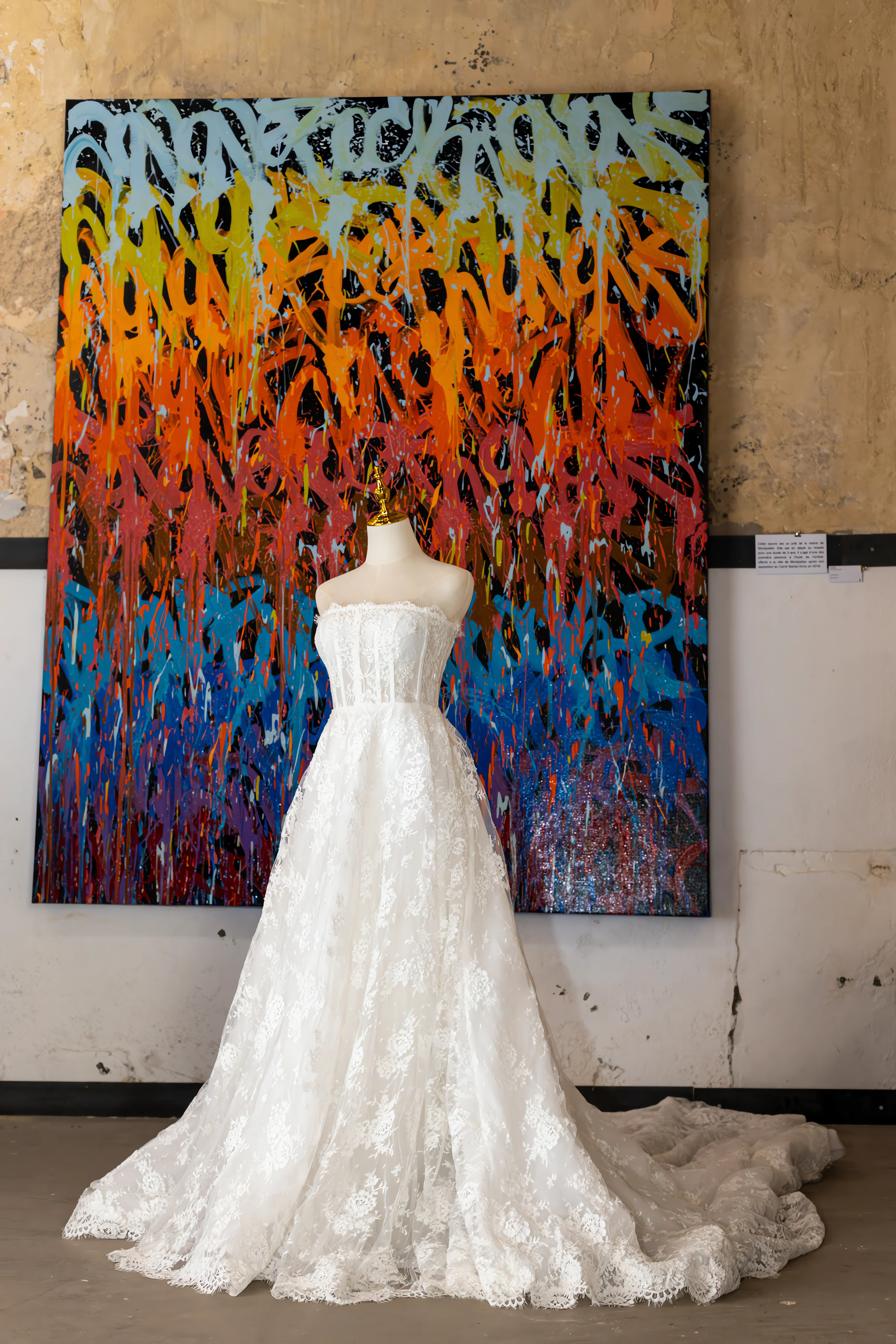 Robe de mariée en dentelle blanche sur mannequin devant une toile de street art colorée et expressive.
