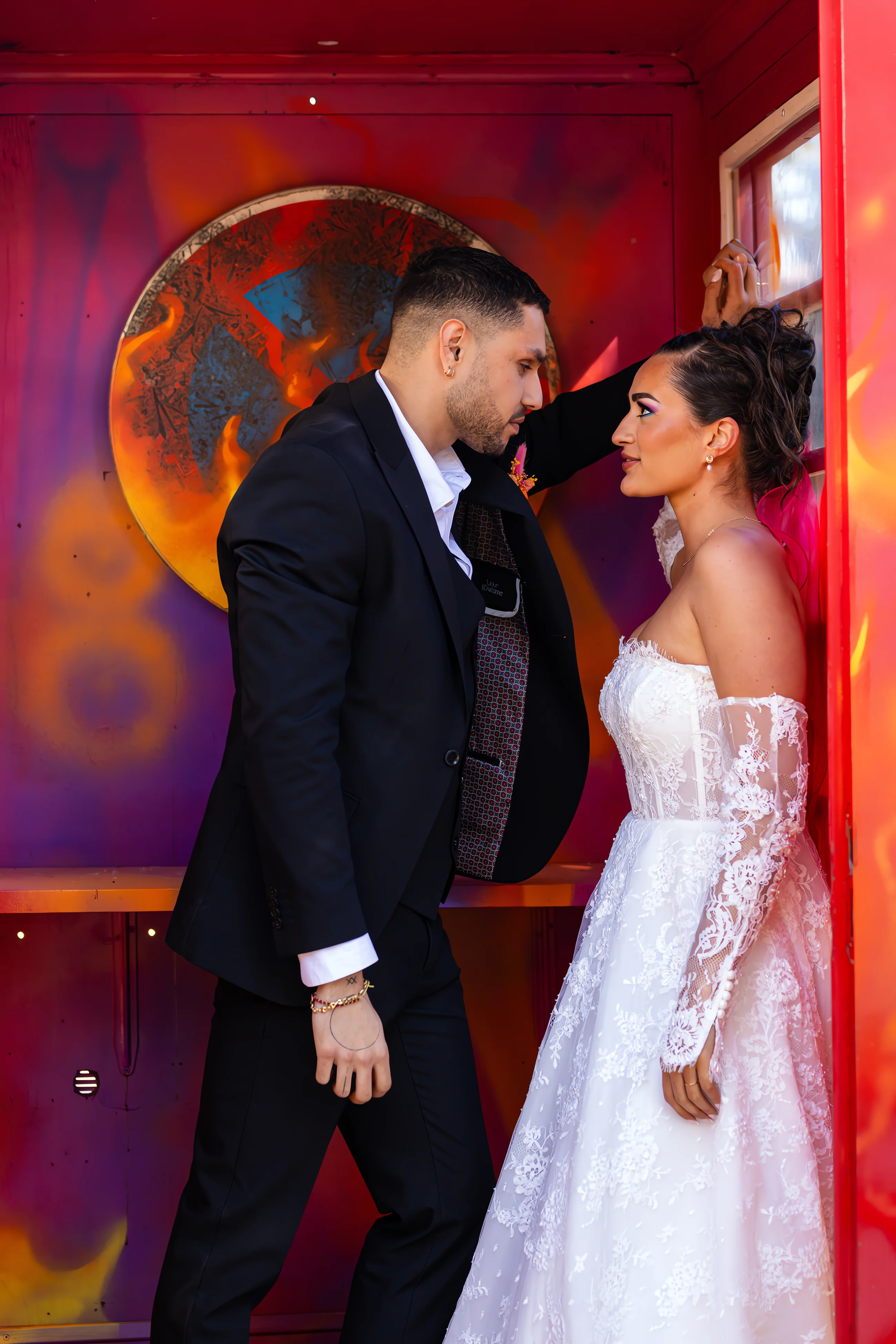 Couple de mariés posant avec complicité devant un mur de street art coloré aux tons rouge, orange et violet.