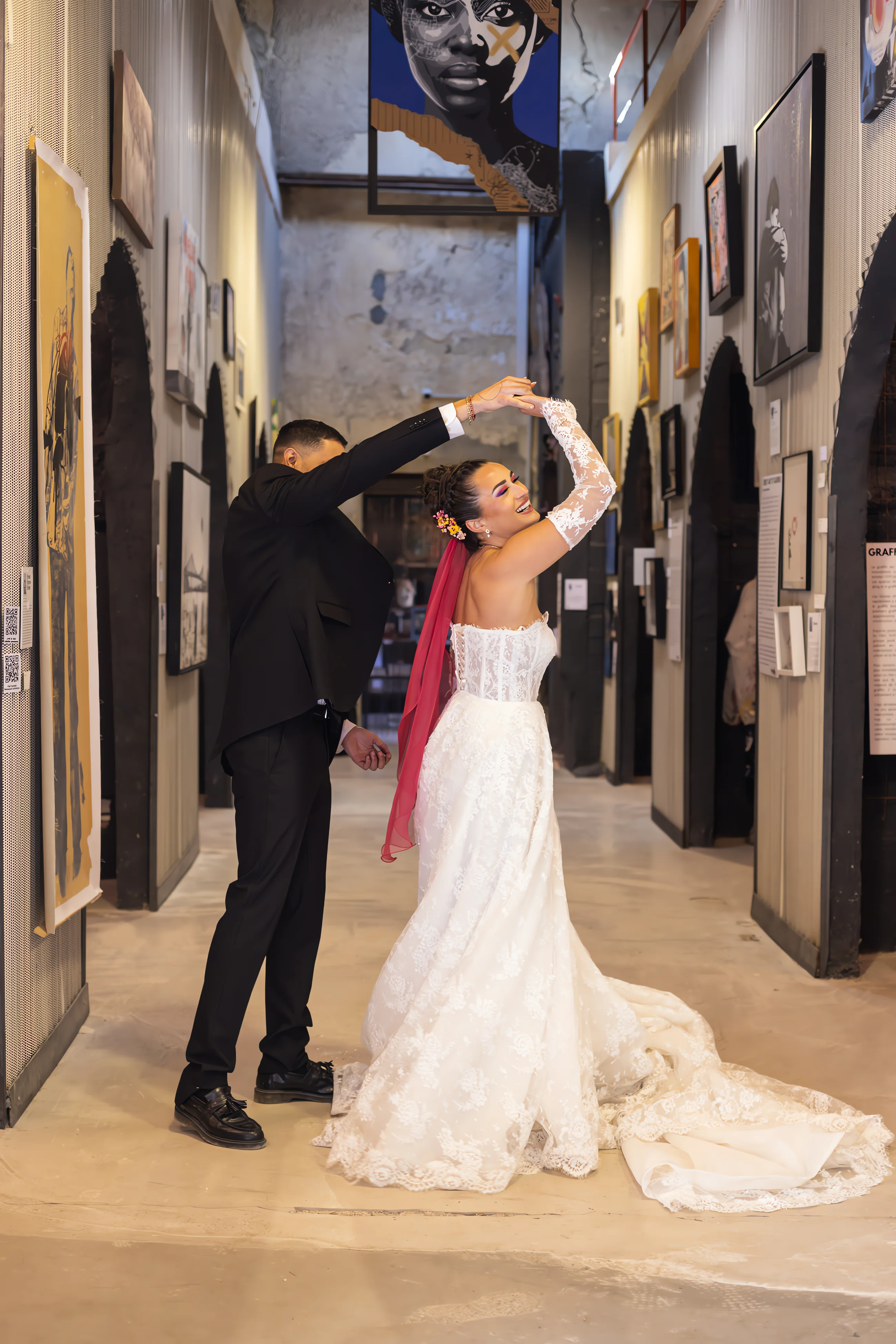 Couple en tenue de mariage dansant dans une galerie de street art industrielle.