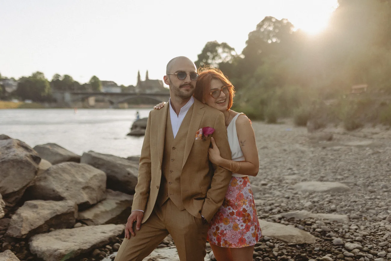 Couple élégant au style rétro posant sur une rive rocheuse au coucher du soleil, ambiance romantique et chaleureuse.