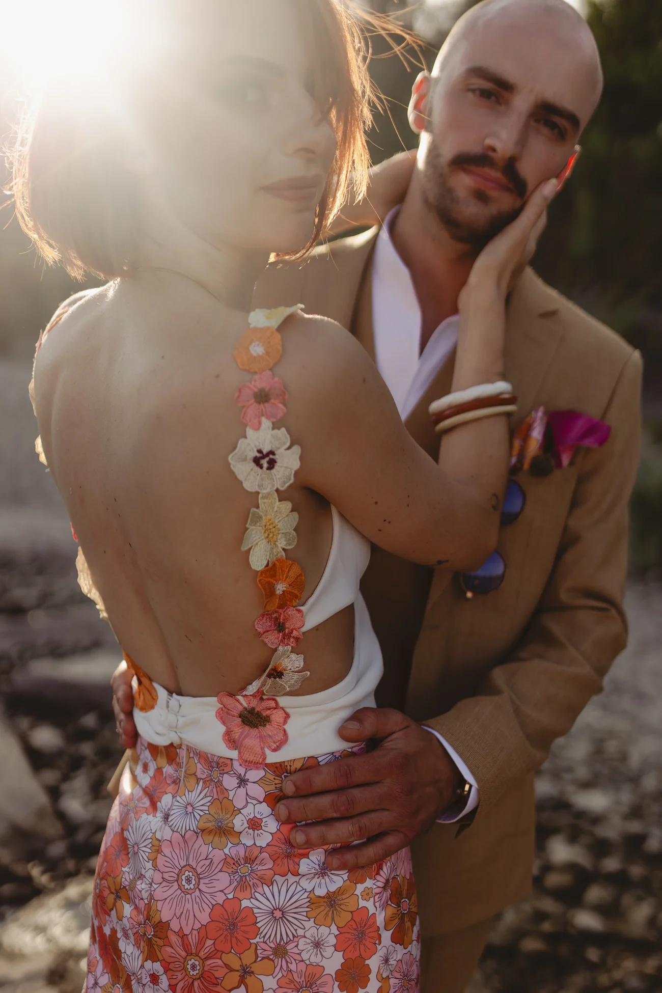 Couple en tenue rétro beige et fleurie s'enlaçant tendrement sous une lumière dorée et romantique.
