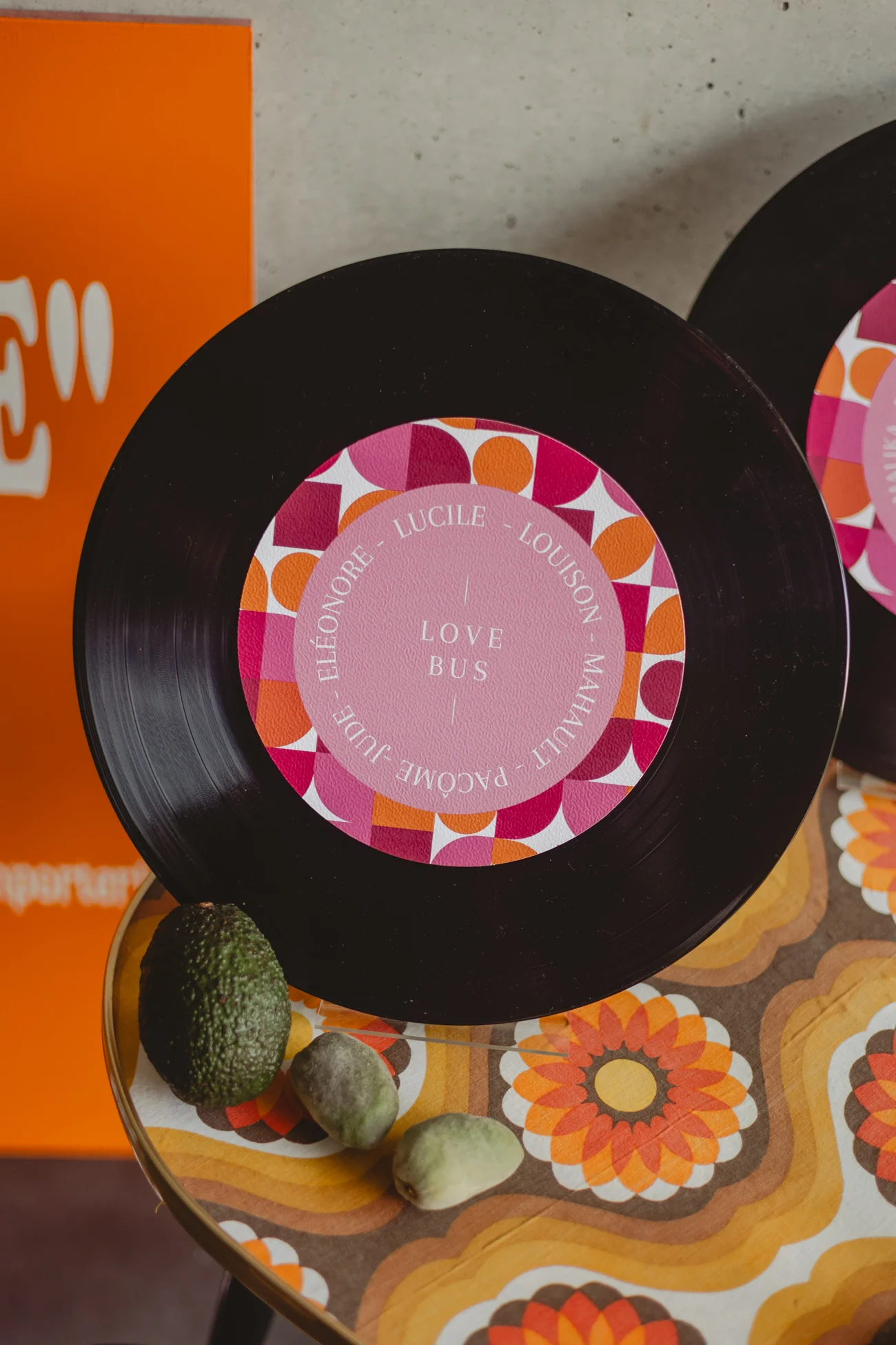 Disque vinyle personnalisé rose et noir posé sur une table aux motifs rétro colorés avec des avocats.
