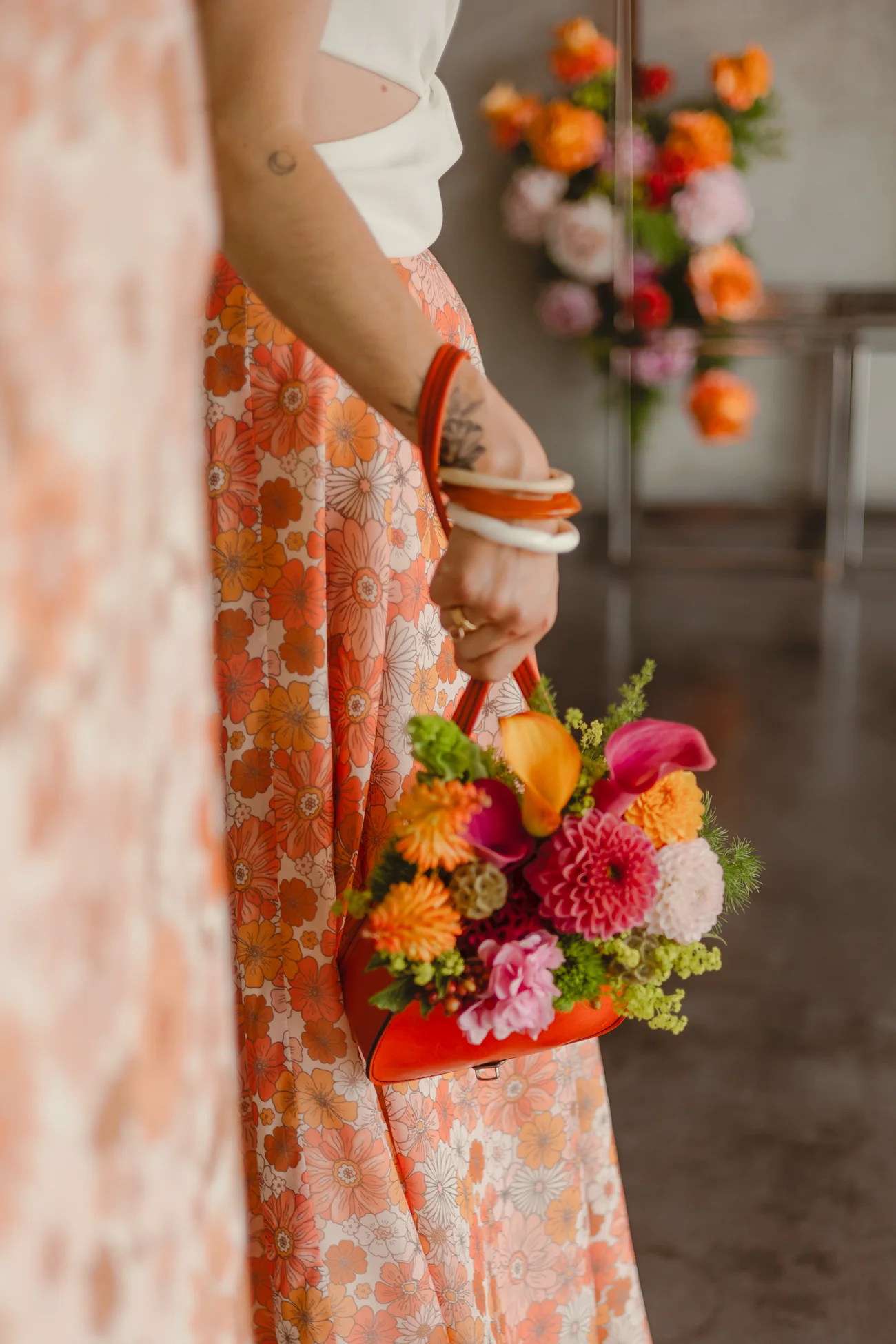 Gros plan d'une femme en jupe fleurie orange portant un sac à main rouge rempli de fleurs colorées.