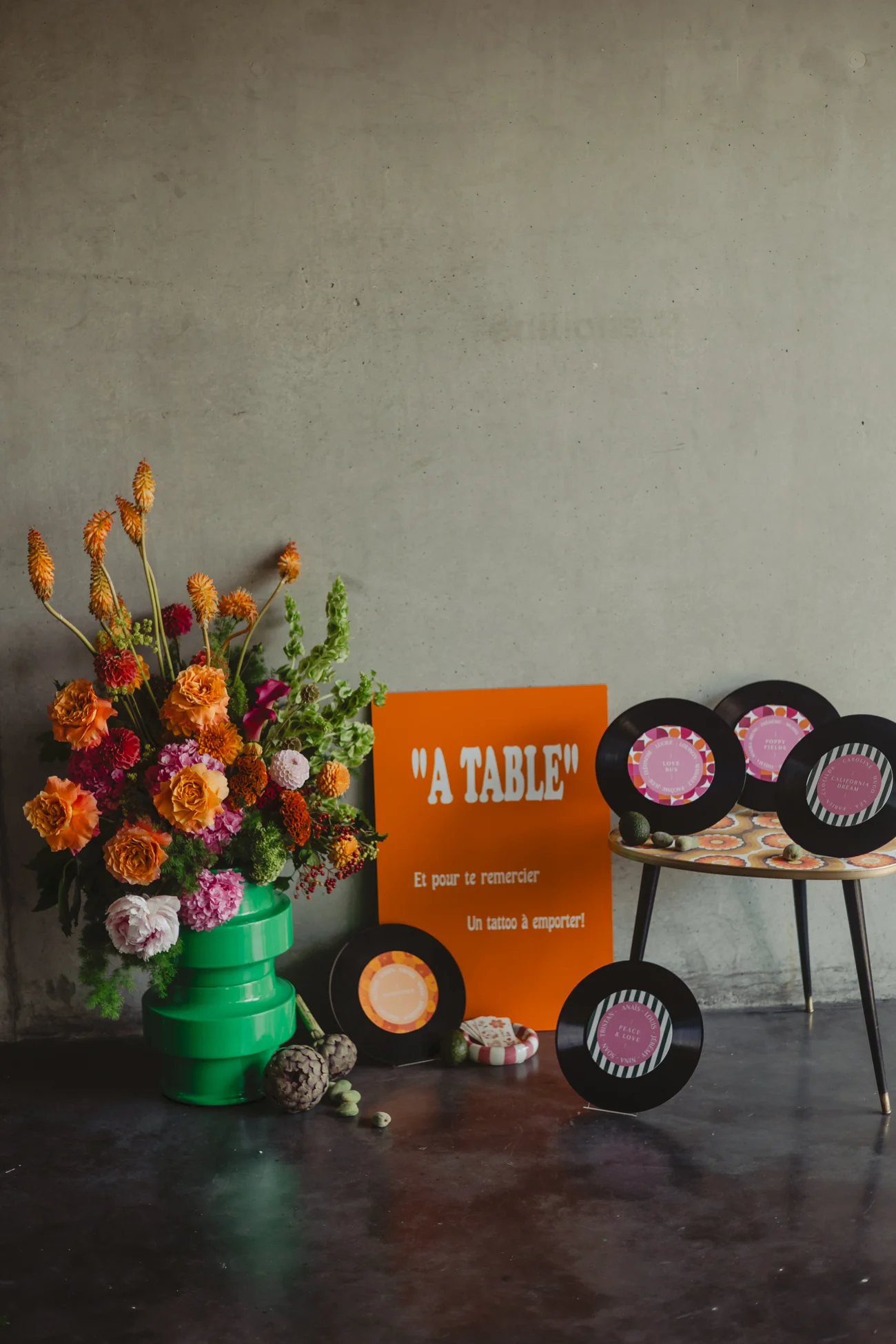 Décoration rétro avec bouquet coloré, vinyles et panneau orange sur fond de mur gris béton.