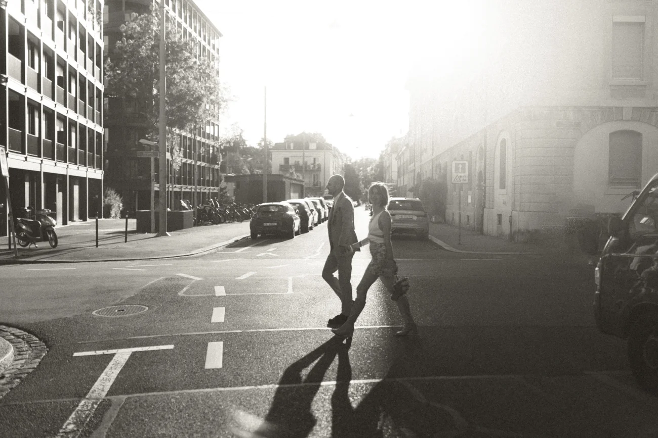 Couple élégant traversant une rue urbaine ensoleillée, photographie en noir et blanc à l'ambiance rétro.