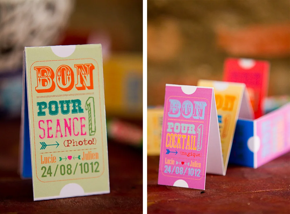 Petits bons de fête foraine colorés et personnalisés pour un mariage, disposés sur une table en bois.