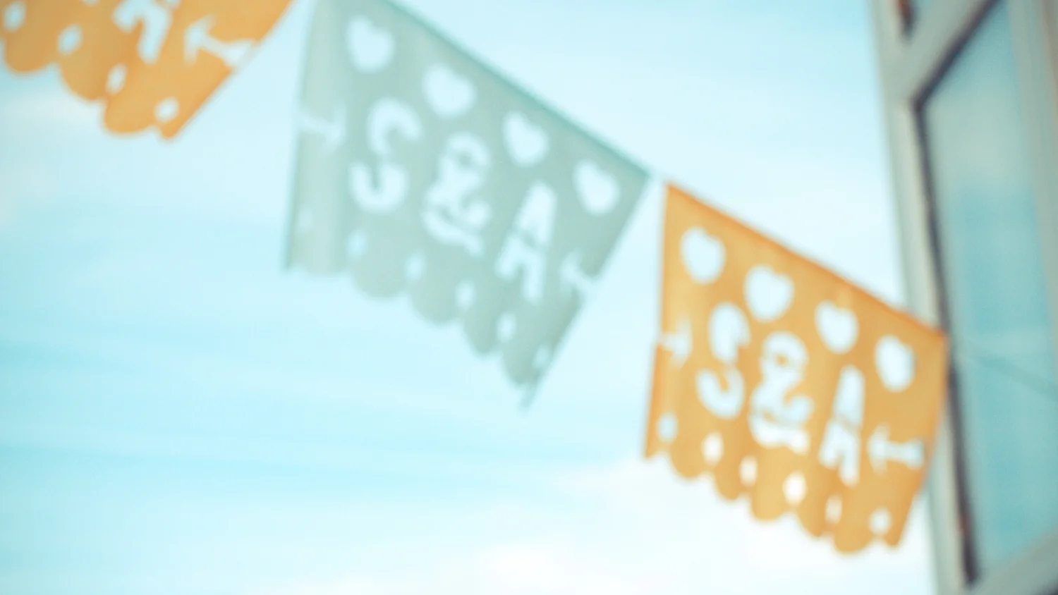 Guirlandes de papel picado orange et blanche avec des initiales, suspendues sous un ciel bleu clair et lumineux.