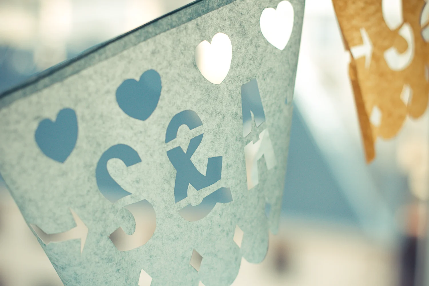 Détail d'une guirlande en papel picado bleu clair avec des cœurs et des lettres découpées dans un style romantique.