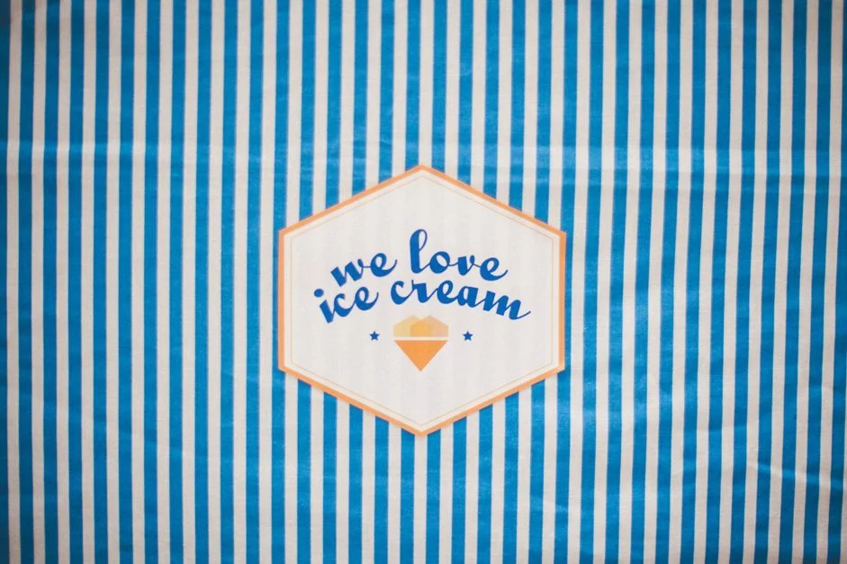 Panneau hexagonal blanc et orange avec l'inscription « we love ice cream » sur un fond à rayures bleues et blanches.