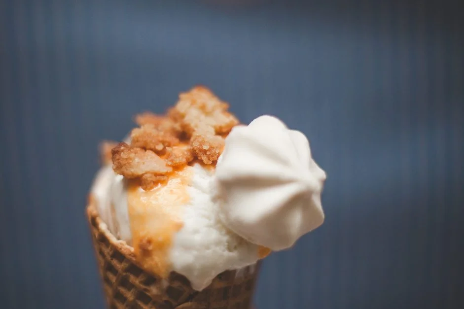 Une glace à la vanille dans un cornet, garnie de crumble doré et d'une meringue blanche sur fond bleu.