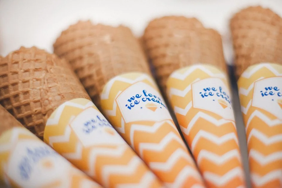 Cornets de glace alignés, enveloppés de papier jaune et blanc à motifs chevrons pour un bar à glaces festif.