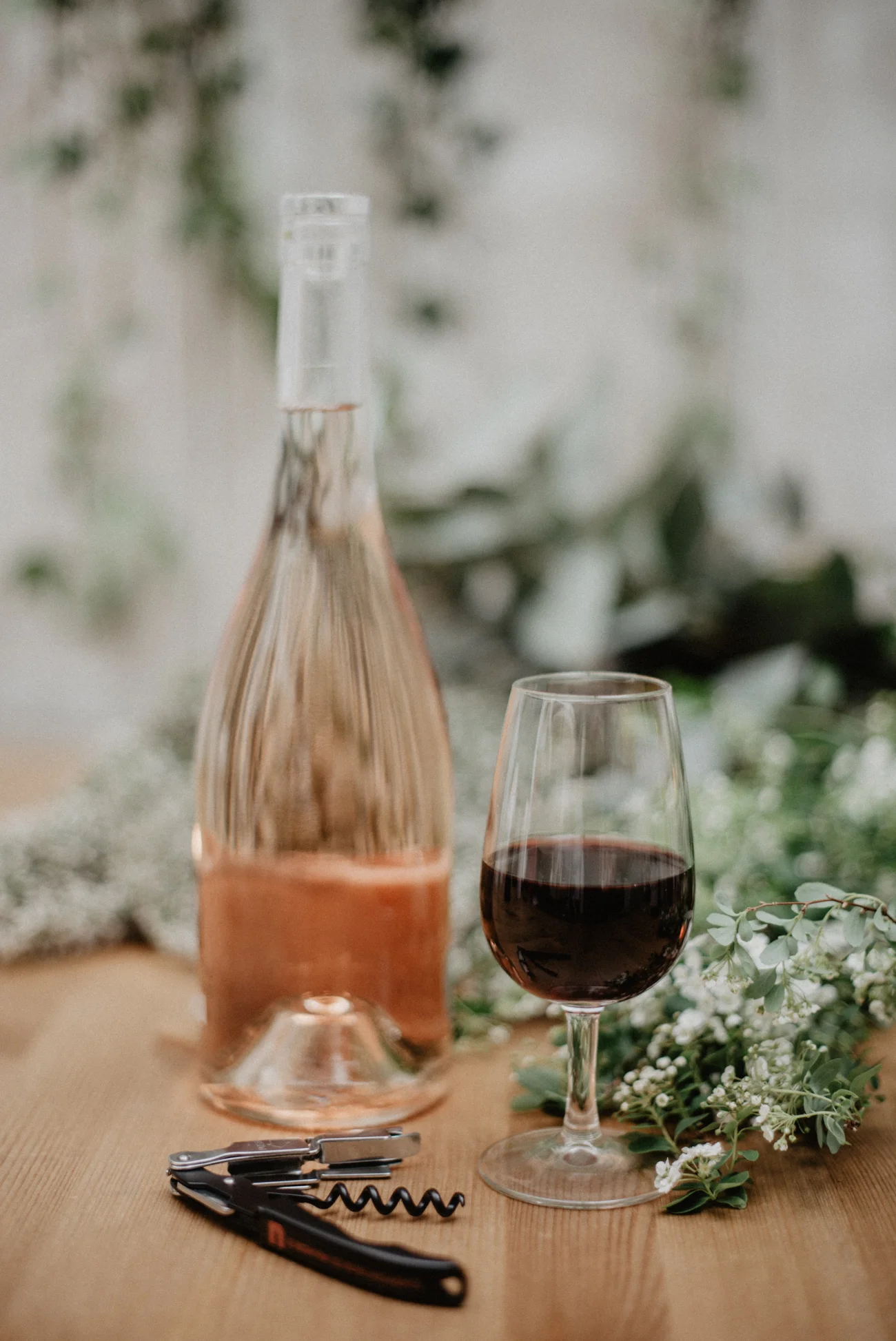 Un verre de vin rouge et un verre de vin rose, accompagnés d'un bouteille et d'un ouvre-bouteille, entourés de fleurs