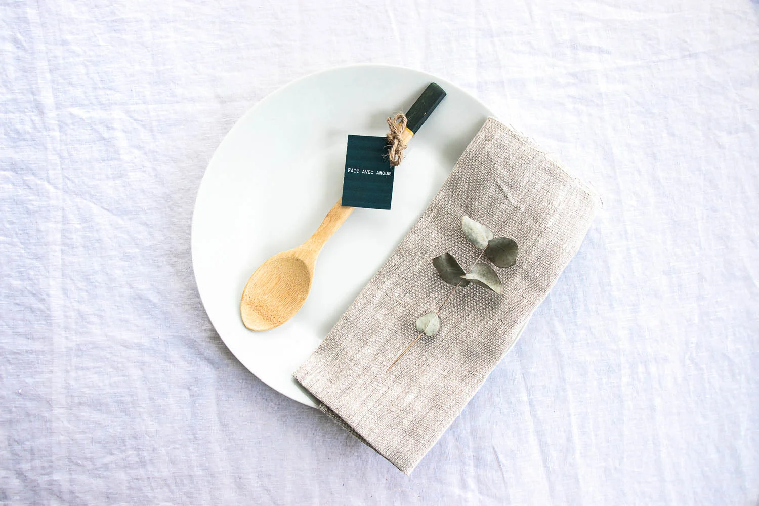 Un plateau blanc avec un fourchette en bois et un serviette textile, accompagné d'une branche de eucalyptus, idéaux