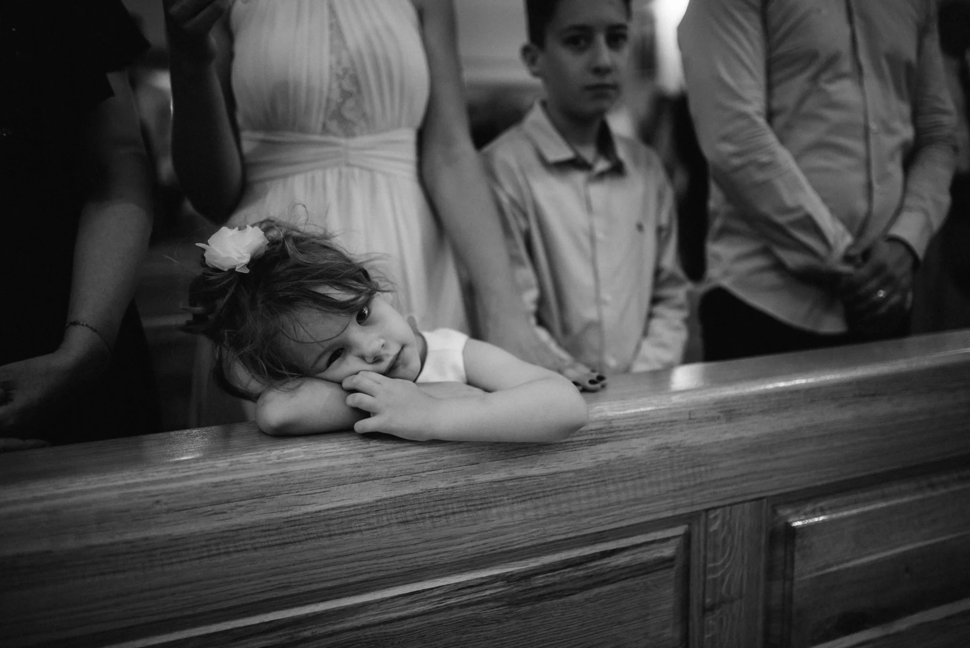 Une jeune fille pensive au parvis d'un mariage, portant un fleur de lis dans son cheveux, sous la surveillance