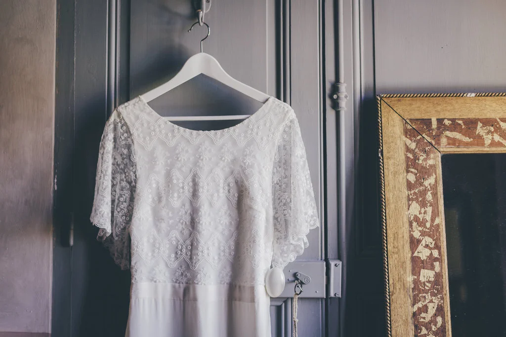 Élégante robe de mariage blanche à manches courtes suspendue sur un arceau, encadrée d'un cadre antique, évoquant un