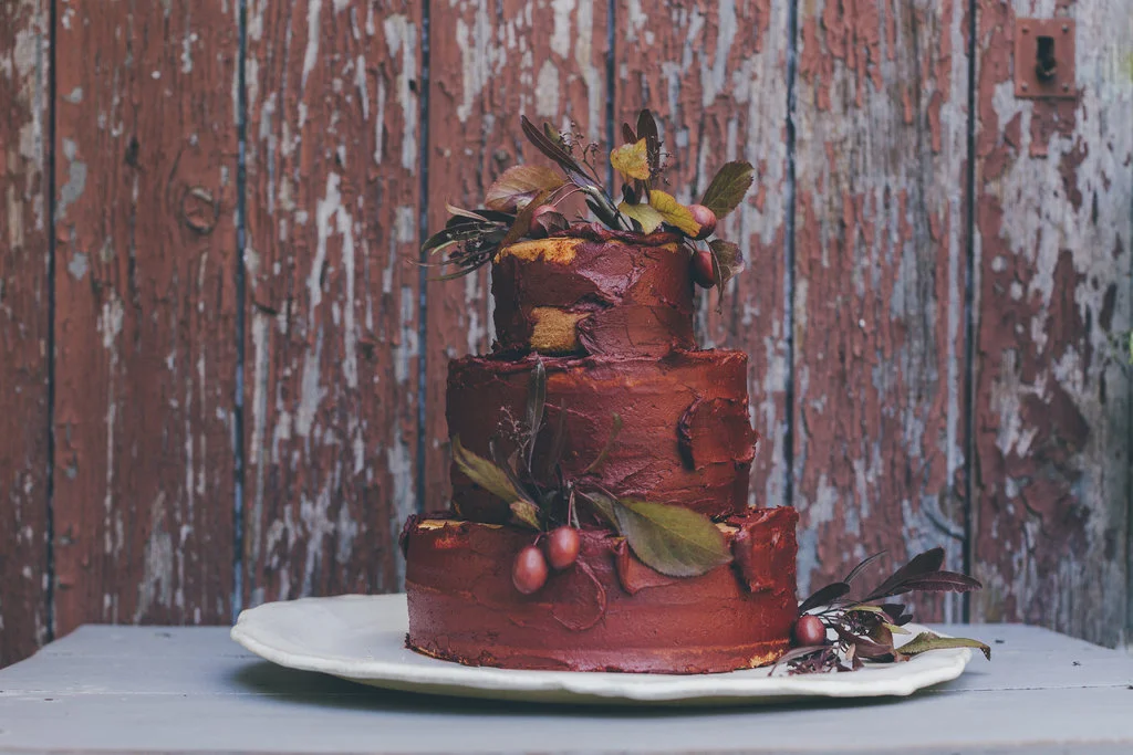 Un gâteau à deux étages orné de feuilles et de baies rouges sur un fond de fonds en bois égratigné, créant un