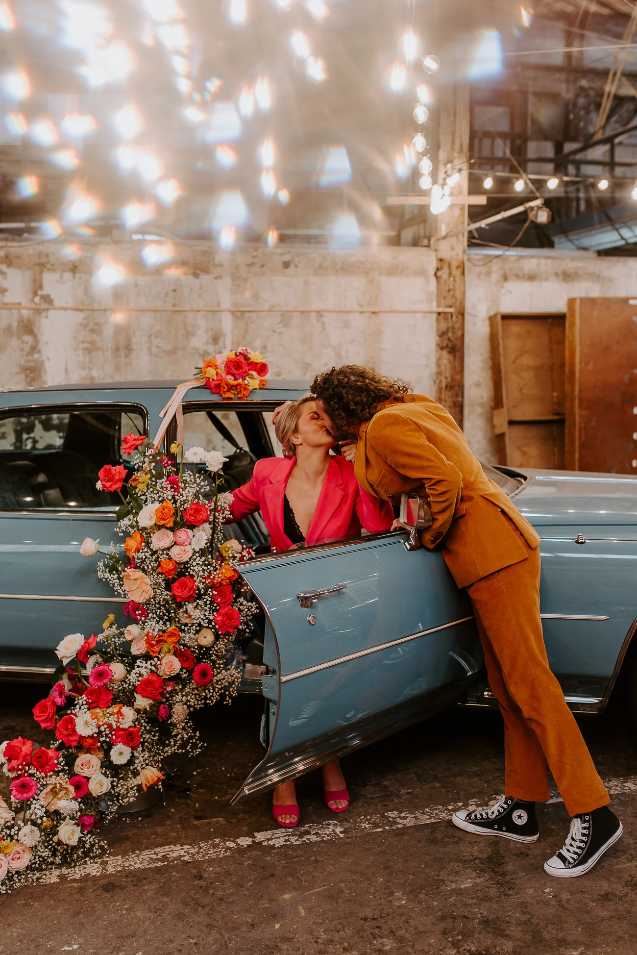 Un couple romantique échange un baiser tendre à côté d'un ancien modèle de voiture rempli de fleurs colorées, échoant