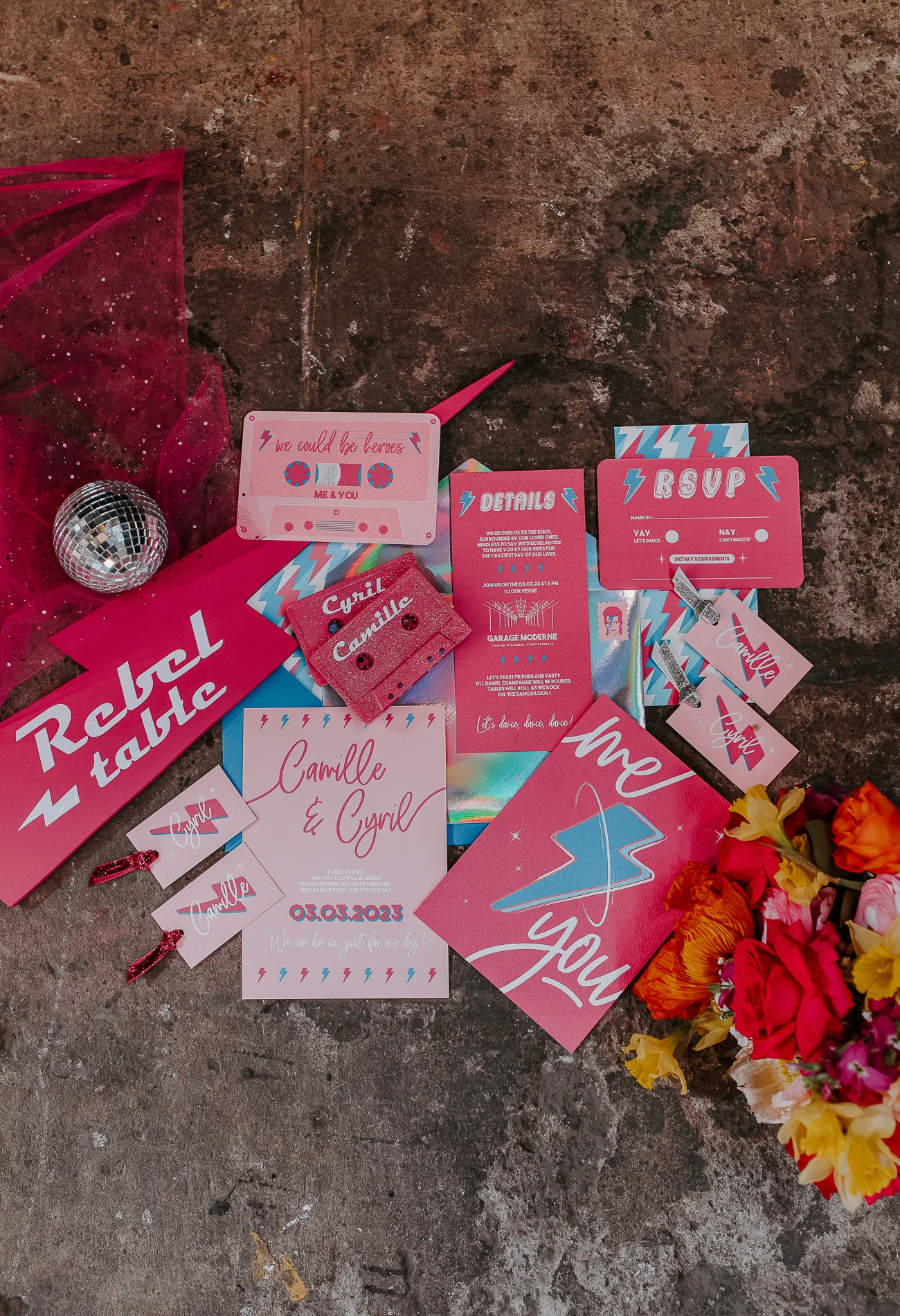 Un coup de fouet de mariage rose Bowie avec des invitations en rose et bleu, un disque de danse et des fleurs colorées.