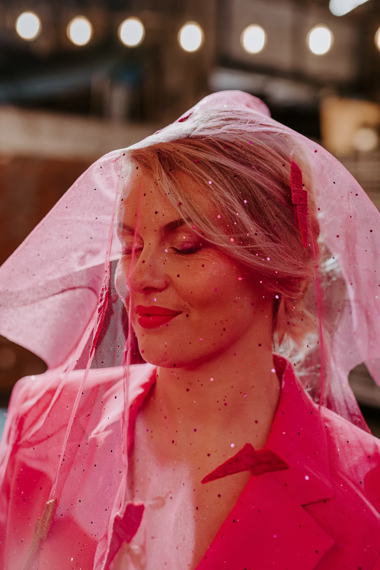 Une mariée dans un manteau rose et une cape en tulle rose avec des perles, évoquant un mariage fantaisiste et coloré.