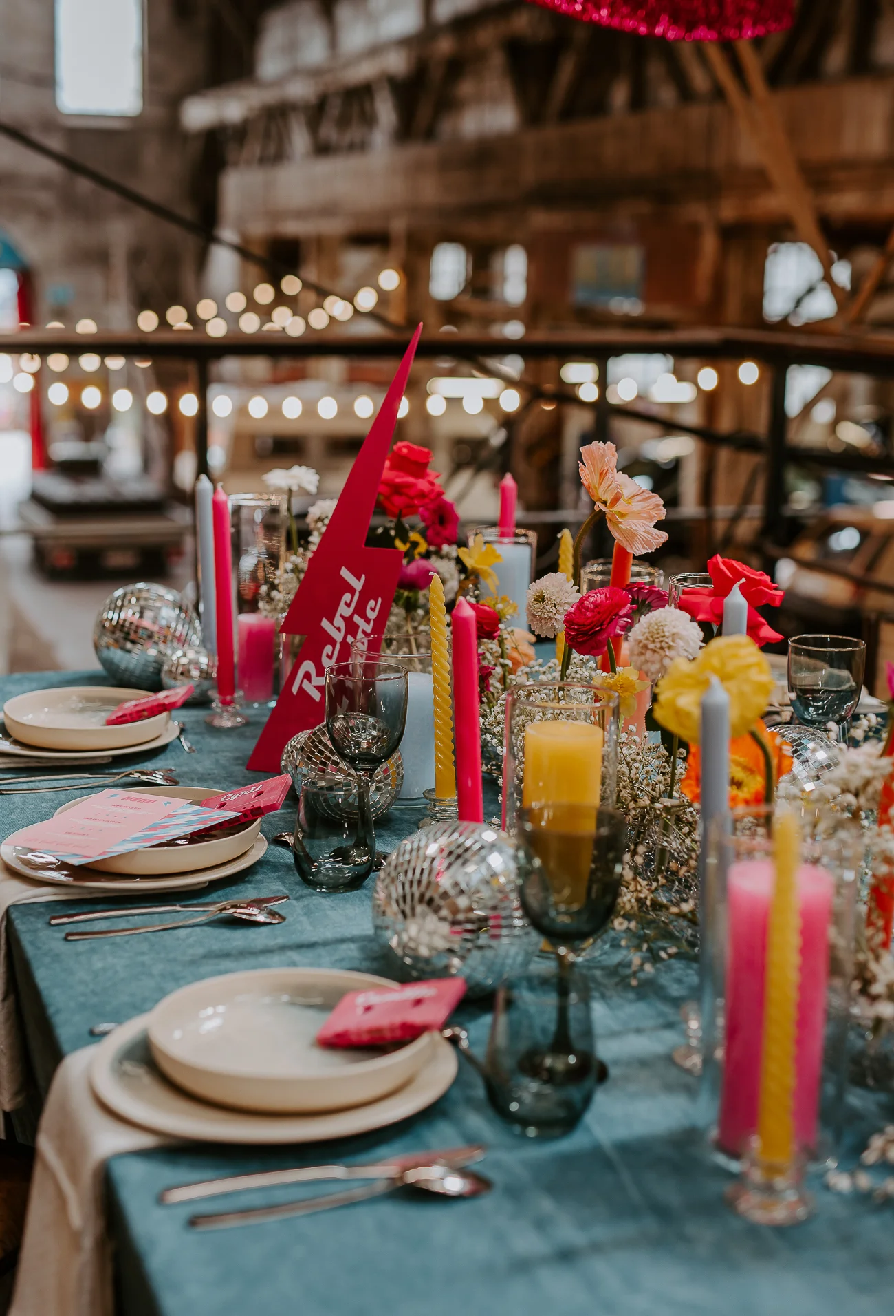 Un banquet intime et coloré dans un décor industriel, avec des fleurs vives et des cierpes pour une ambiance romantique.