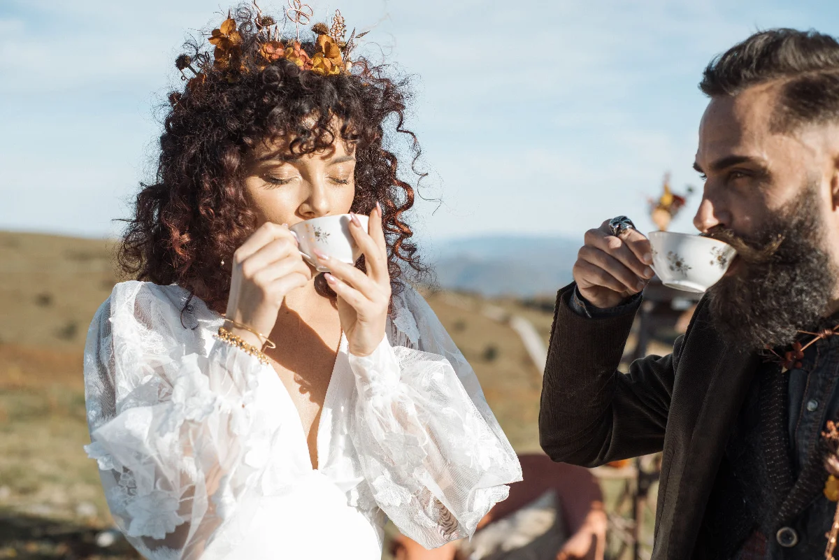 Couple en tenue folk buvant du thé dans des tasses en porcelaine, en plein air, dans une ambiance bohème et naturelle.