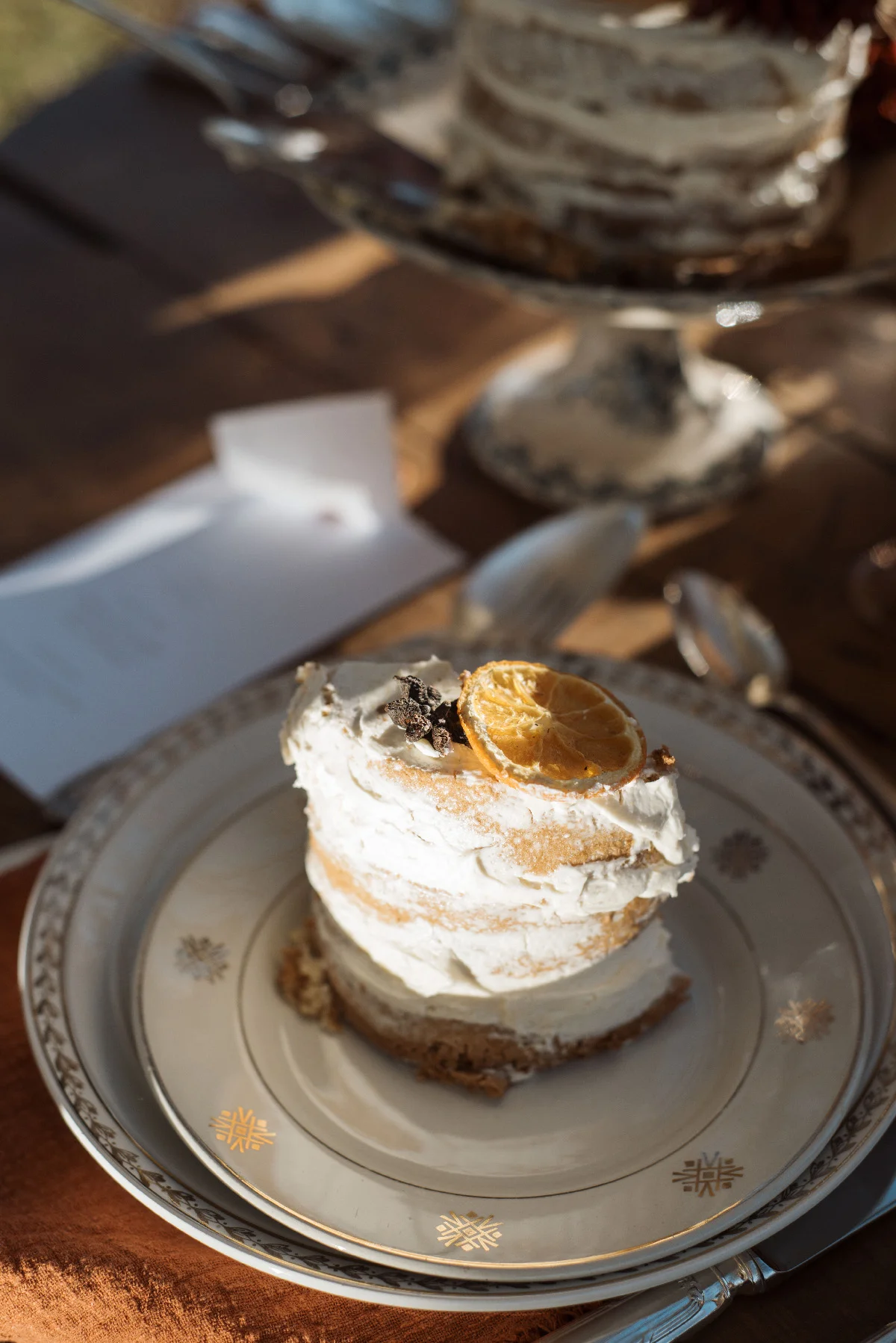 Une part de gâteau rustique à la crème et tranche d'orange sur une assiette vintage, ambiance mariage folk et naturelle.