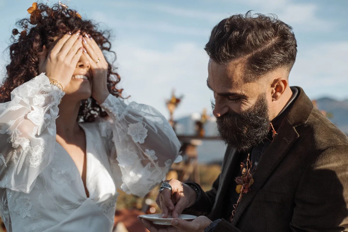 Un marié barbu présente une bague à sa future épouse aux yeux bandés lors d'un mariage folk en plein air.