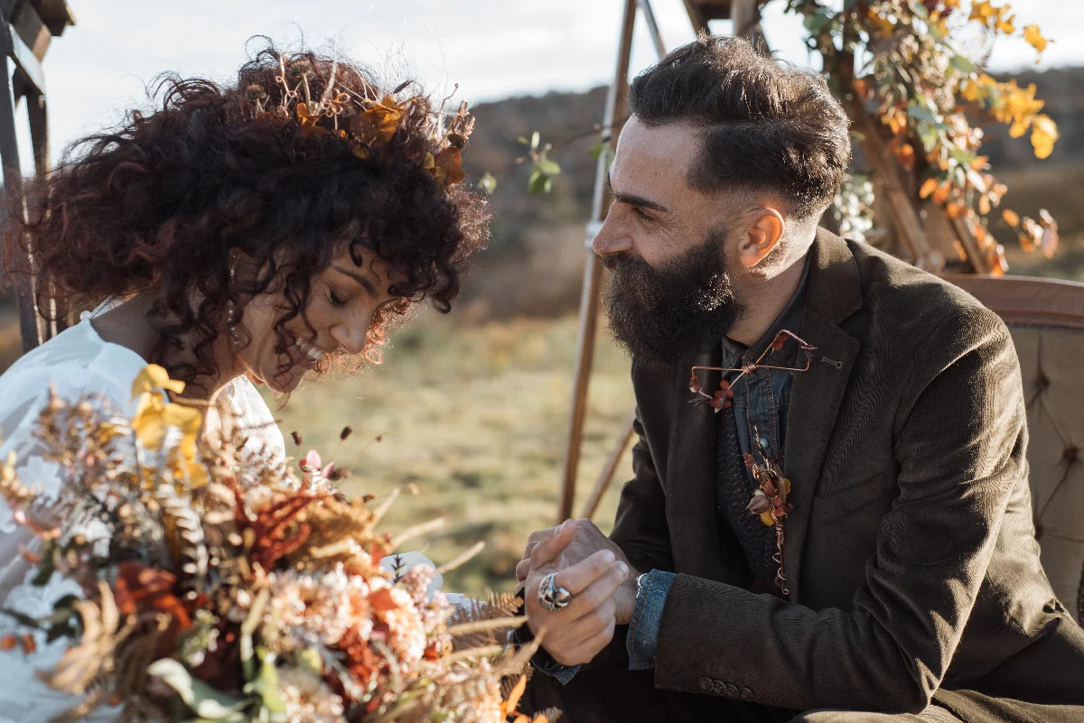 Couple en tenue folk s'enlaçant tendrement en extérieur avec un bouquet automnal et des tons terreux.