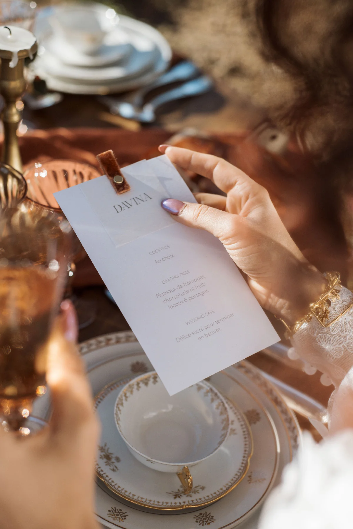 Main tenant un menu blanc personnalisé sur une table élégante aux tons chauds et dorés.
