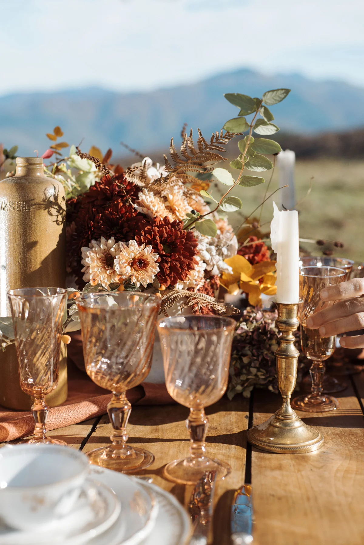 Table rustique avec fleurs automnales, verres ambrés et bougies, dans un décor naturel et chaleureux.