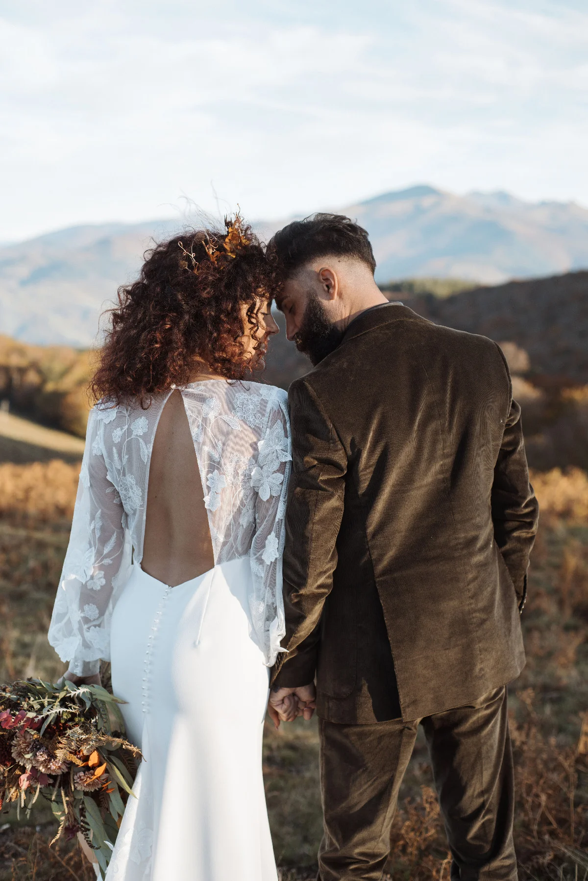 Couple de mariés en tenue folk se tenant par la main face aux montagnes dans une ambiance naturelle et romantique.