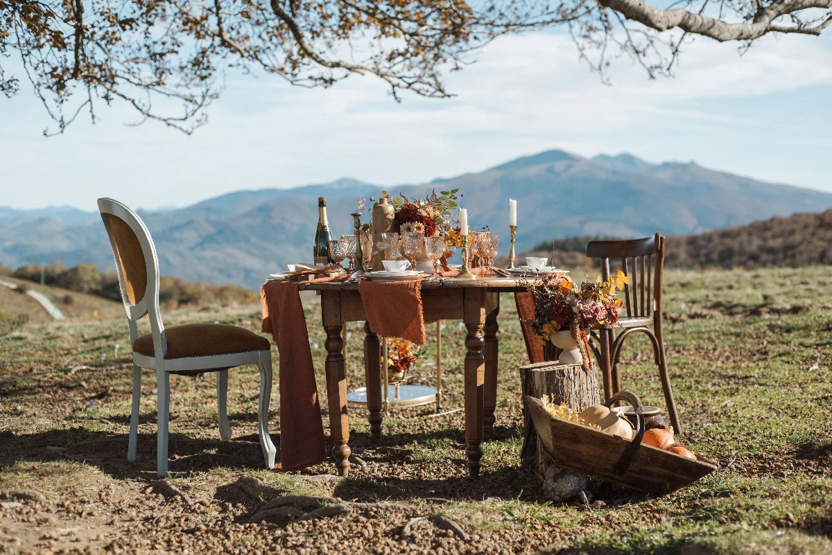 Table dressée dans des tons automnaux pour un dîner romantique en plein air face aux montagnes.