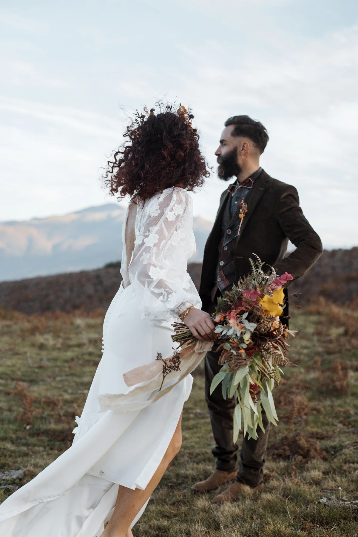 Couple en tenue folk, elle en robe blanche et lui en costume brun, posant en pleine nature avec un bouquet automnal.