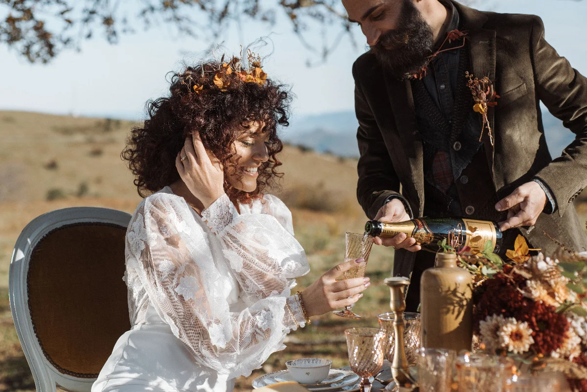 Couple en tenue folk célébrant leur mariage en plein air avec du champagne dans un décor automnal et naturel.