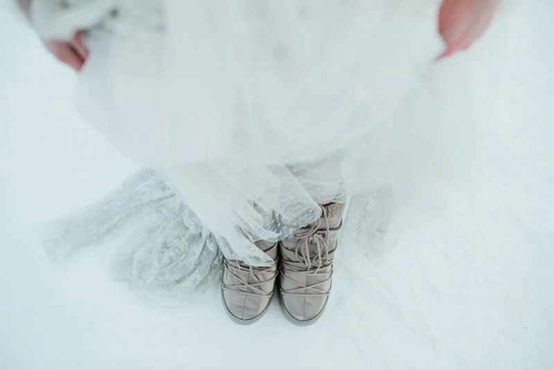 Gros plan sur des baskets dorées sous une robe de mariée blanche et dentelée posée sur la neige.