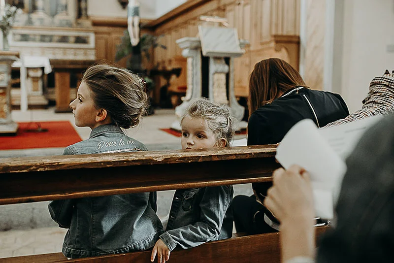 Deux fillettes en vestes en jean assises sur un banc d'église en bois lors d'une cérémonie solennelle.