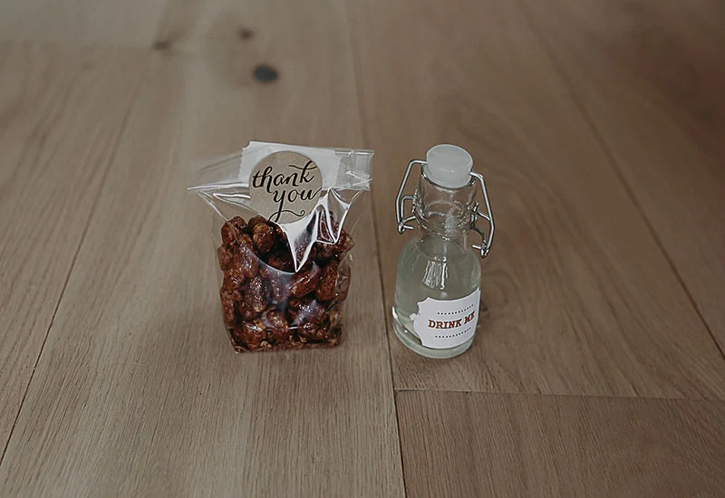 Sachet de noix caramélisées et petite bouteille d'eau étiquetée sur un fond en bois clair.