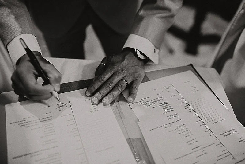 Gros plan en noir et blanc d'un homme signant un registre de mariage avec un stylo.
