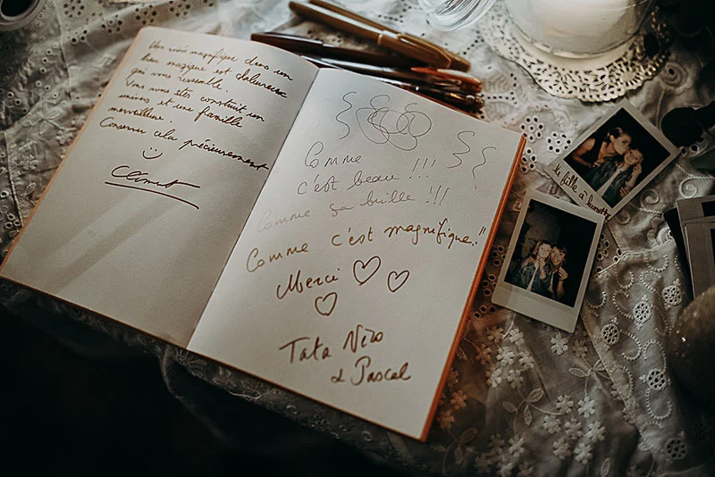 Livre d'or ouvert avec messages manuscrits et photos Polaroid sur une nappe en dentelle blanche, ambiance romantique.