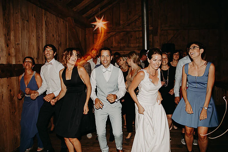 Invités souriants dansant dans une grange en bois lors du mariage de Morgane et Alain, ambiance festive et chaleureuse.