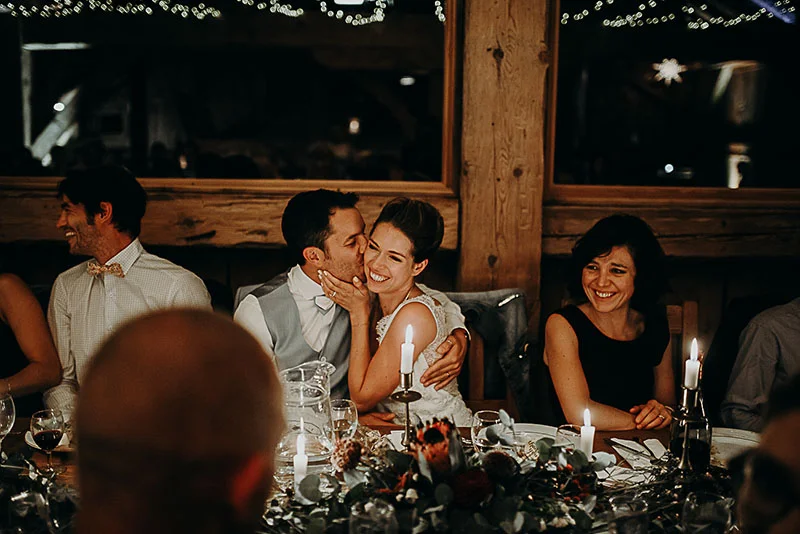 Jeunes mariés complices et invités souriants lors d'un dîner de mariage chaleureux et tamisé.